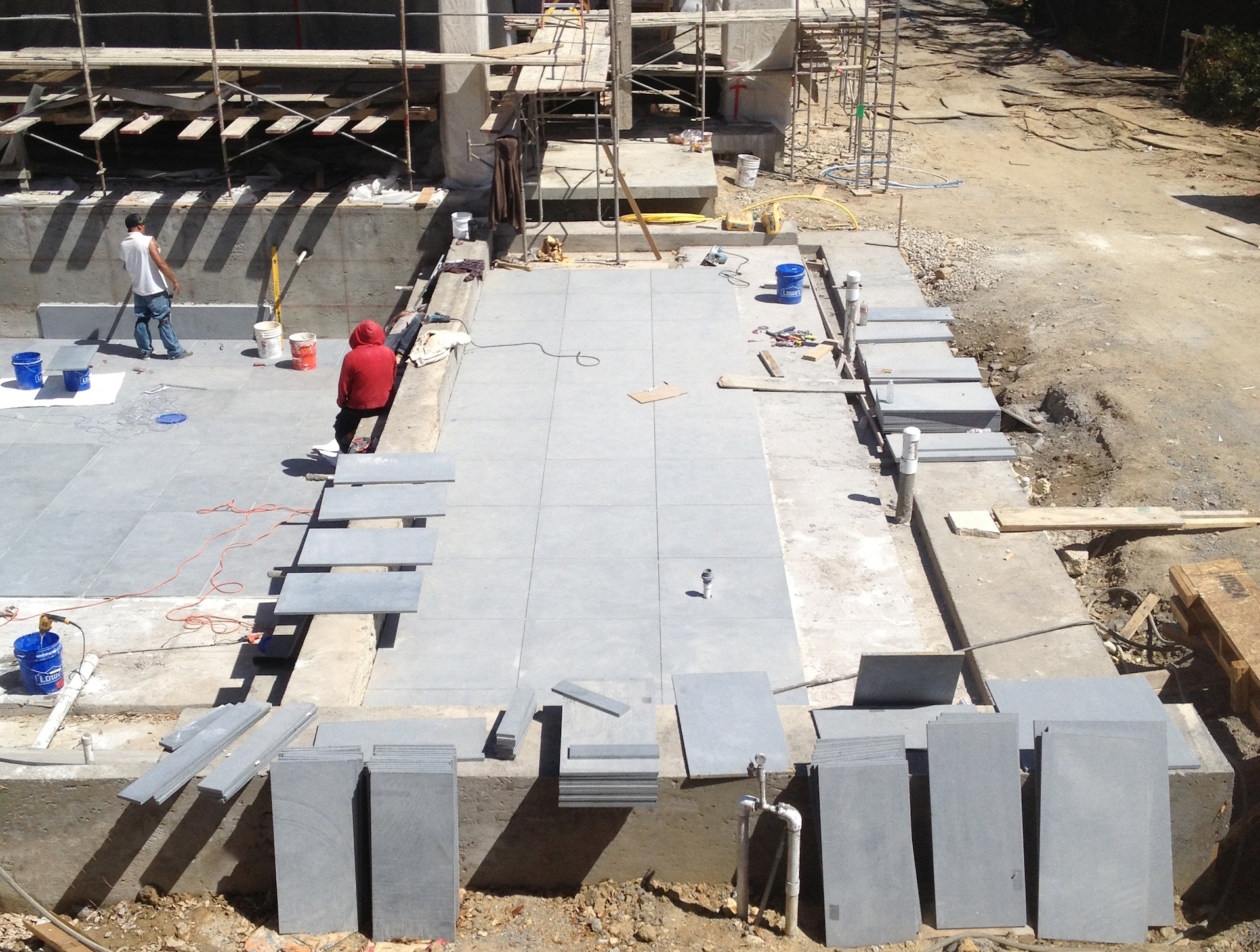 Workers laying a 3' x 3' paving grid for black granite slabs.