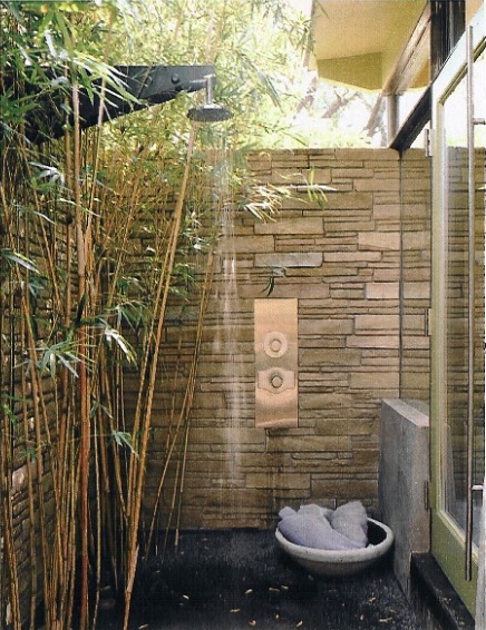 Outdoor shower with stone walls and bamboo plants.