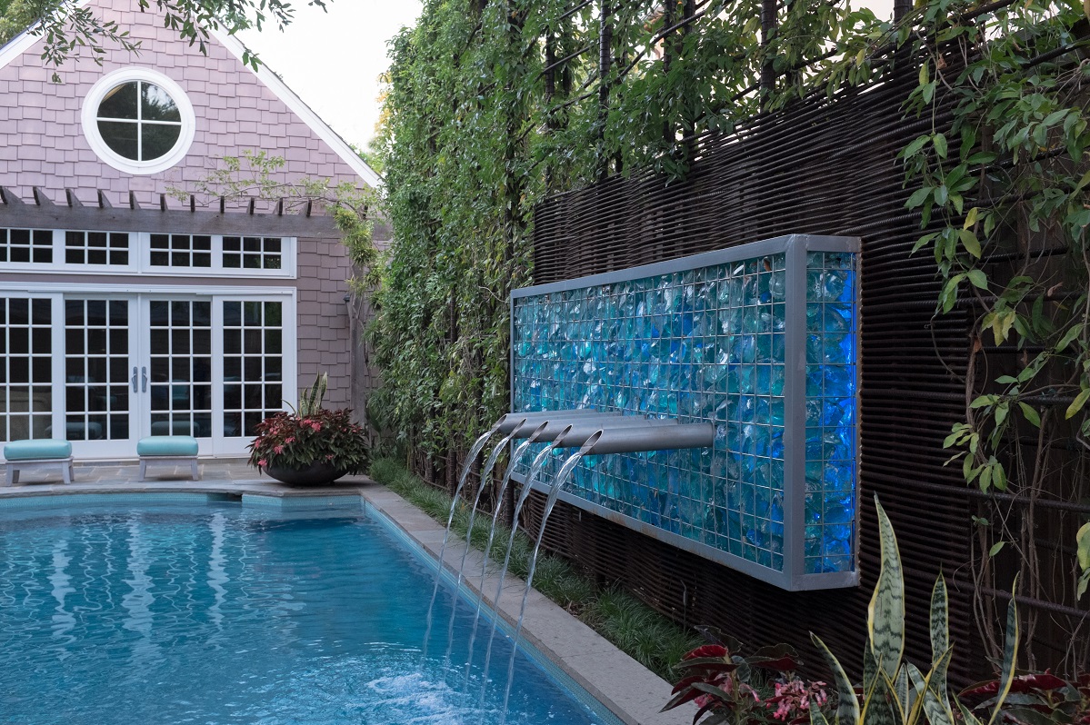 Modern water feature made of steel cage, blue slag glass and scupper mounted on a woven rebar wall.