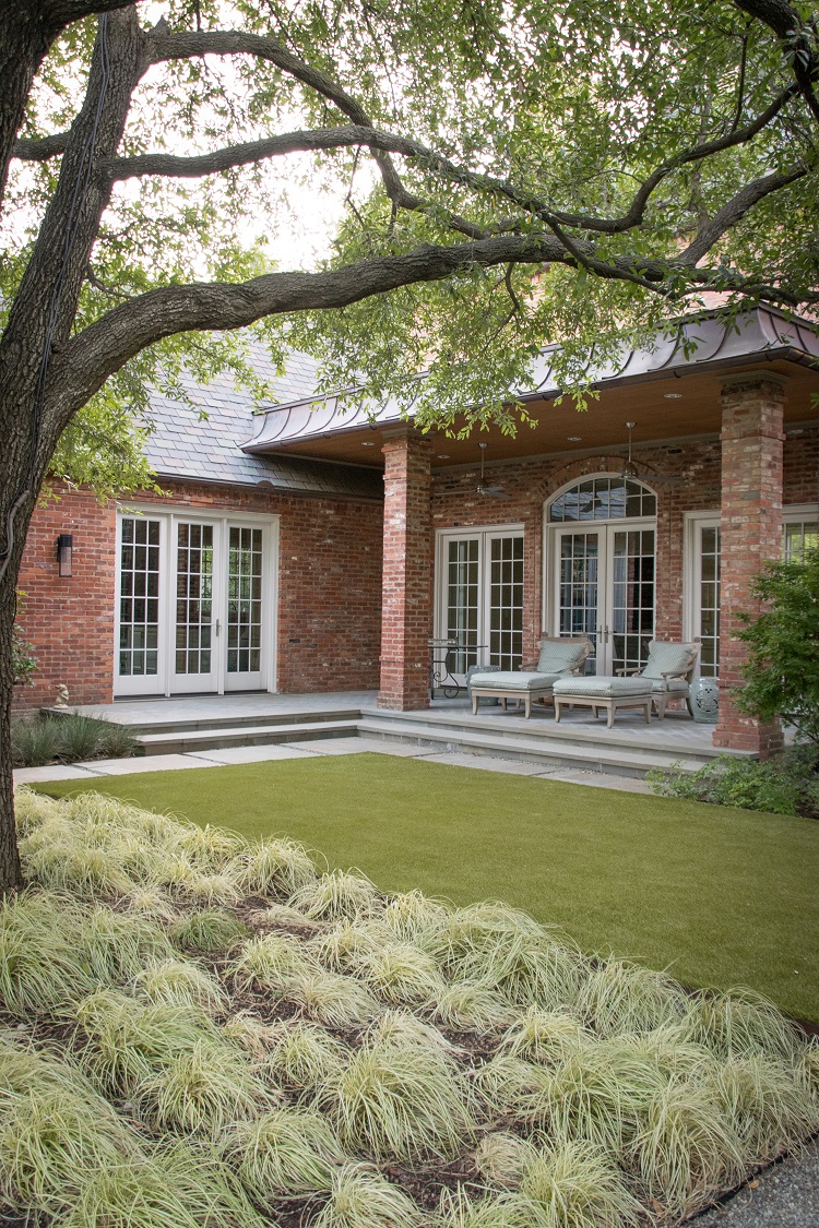 Backyard landscaping features synthetic turf under large live oak tree.