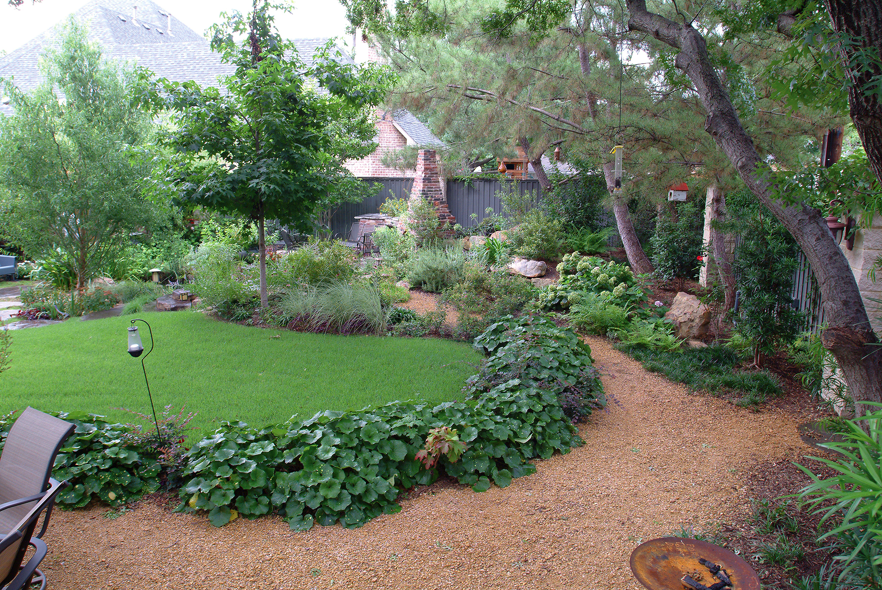 A large pathway of decomposed granite flanked with plants snakes through a natural-looking and lush backyard and garden in Dallas, Texas.