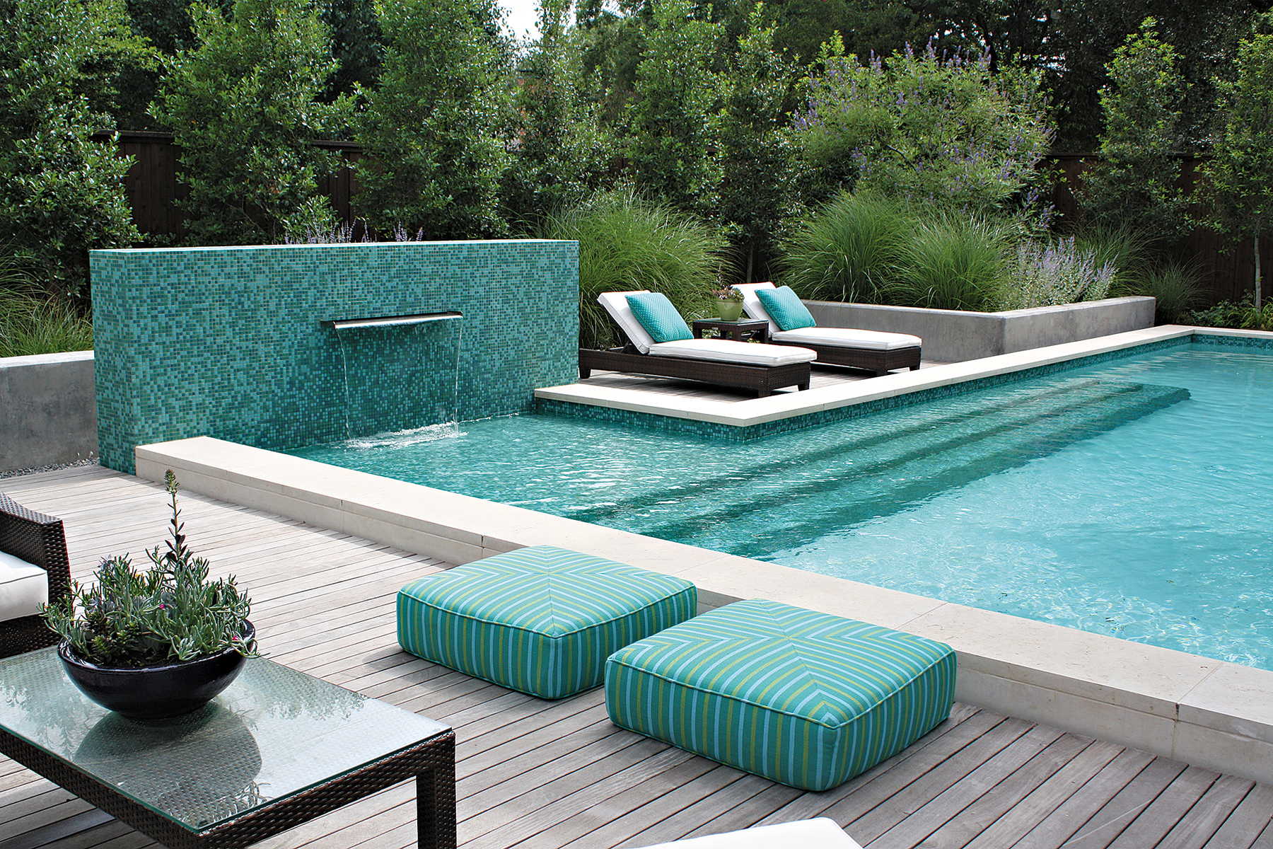 Custom designed Dallas pool has mosaic tile wall and fountain in blues and greens with ipe wood deck, sunbathing area and long steps leading into the shallow area of the swimming pool.