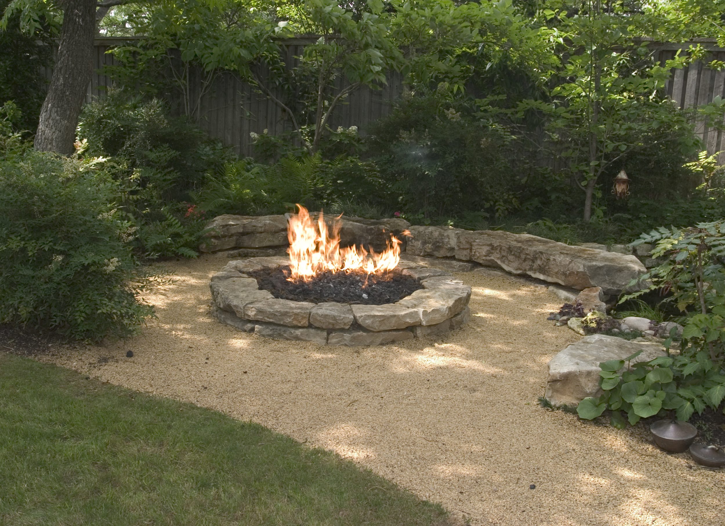 Outdoor fire pit surrounded by a crushed marble path is situated in a garden.