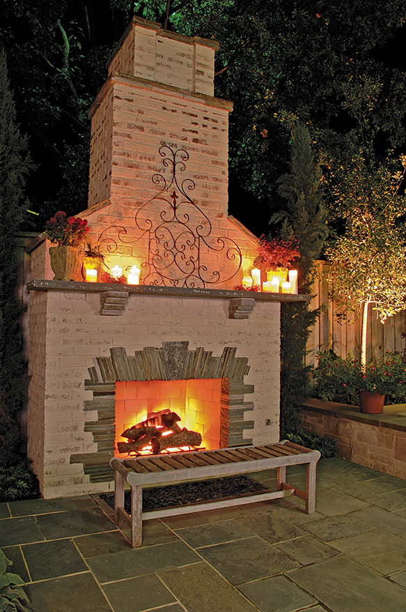 Brick and stone outdoor fireplace shown at night with fire in it.