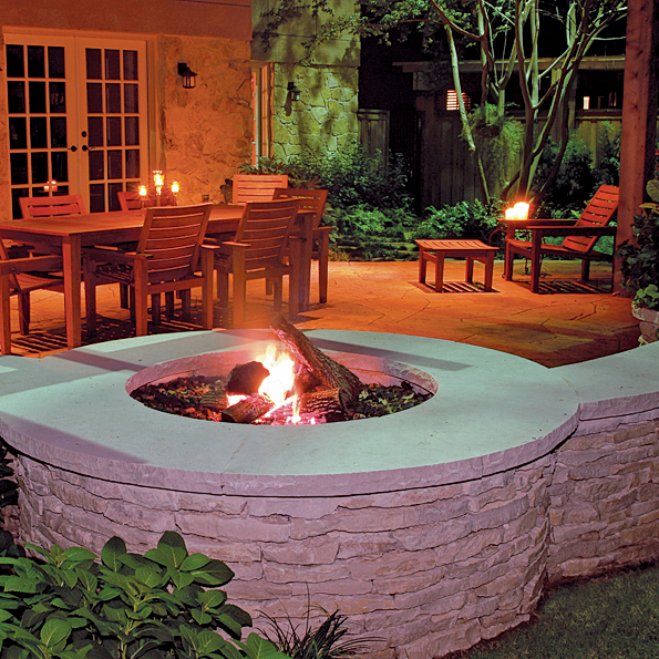 Outdoor fire pit next to outdoor dining area beneath an arbor, shown at night.