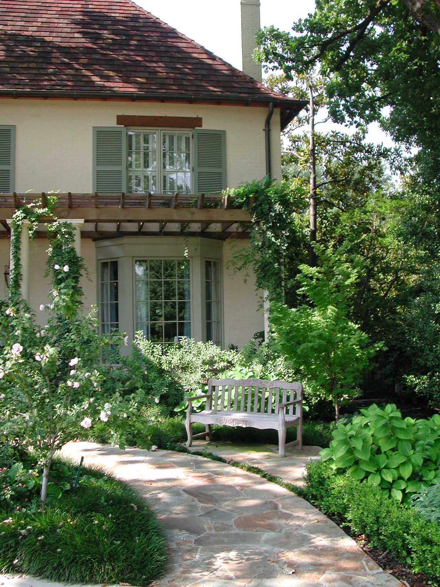 Dallas area home backyard with beautiful trees, shrubs, plants and a bench and walkway.