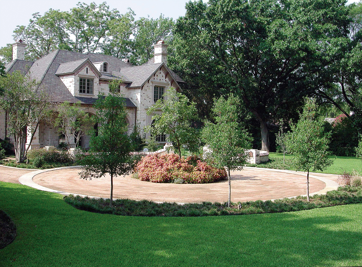 Large circular driveway made of decomposed granite with small garden in the center in front of tradtional two-story residence in Dallas, Texas.