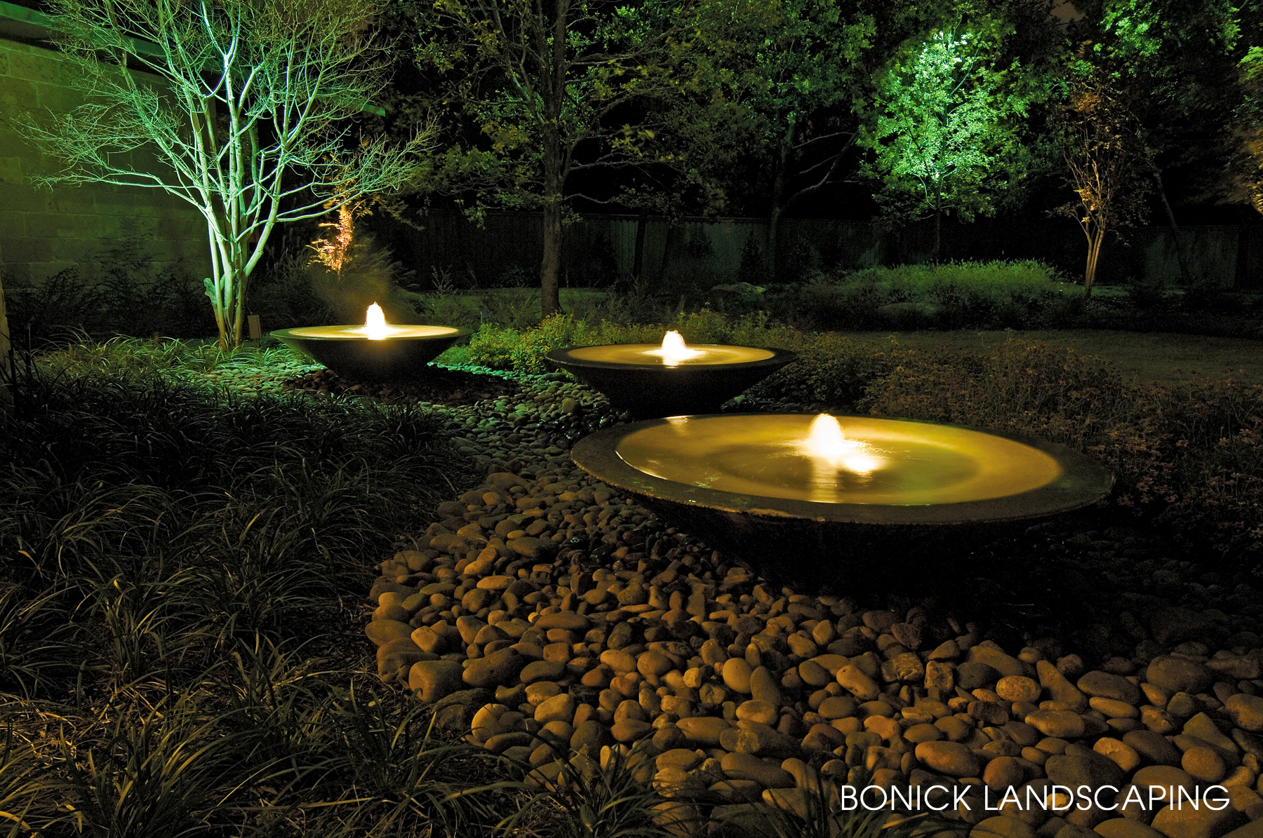 Landscape lighting dramatically lights tree and fountains.