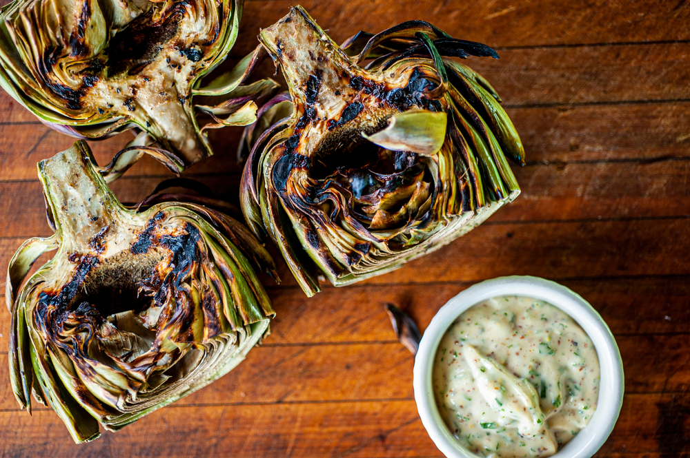 Grilled artichokes with aioli on wood cutting board