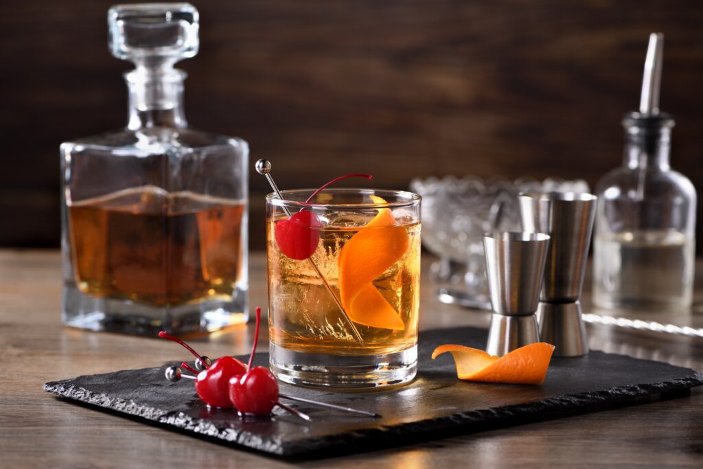 Old Fashioned cocktail on bar with maraschino cherries and orange rind
